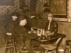 Three men in vintage attire playing cards at a wooden table in a dimly lit room.