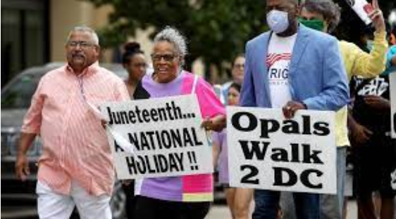 Three people walking with signs advocating for Juneteenth as a national holiday.