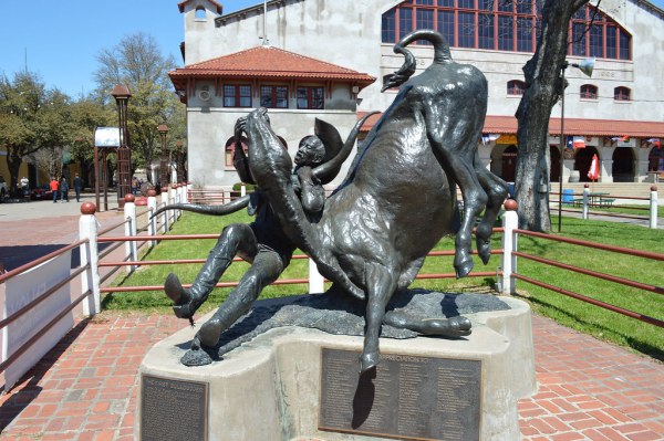 Bronze statue of a man wrestling a bull in a plaza with buildings in the background.