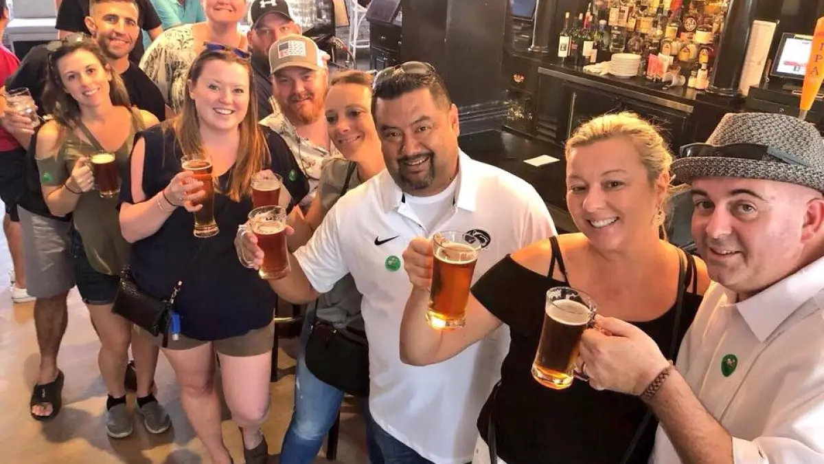 Group of people smiling and holding beer glasses in a bar setting.