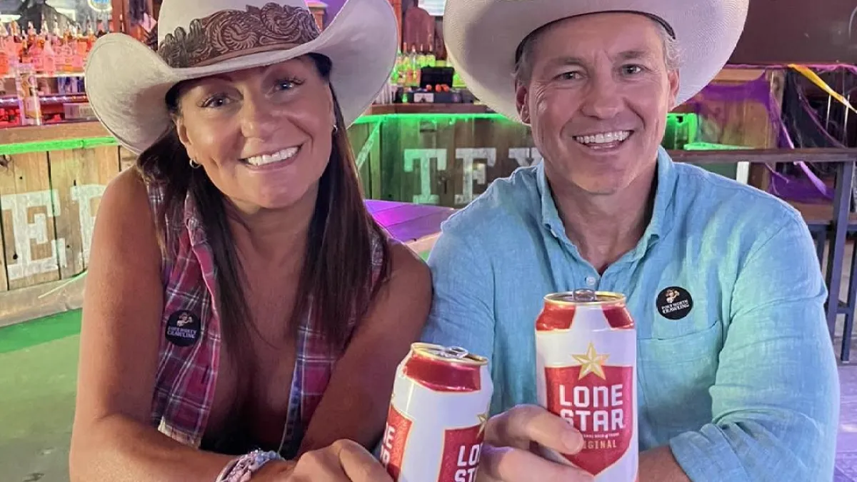 Two people in cowboy hats holding Lone Star beer cans at a bar.
